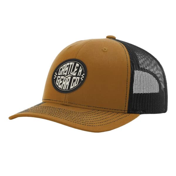 Introducing the Ollie Snapback Hat: This stylish trucker hat features a curved brim and a unique design. The front panel is brown, adorned with a black patch in the center showcasing the white text "Castle X Gear Co." For added comfort and ventilation, the sides and back are crafted from black mesh.